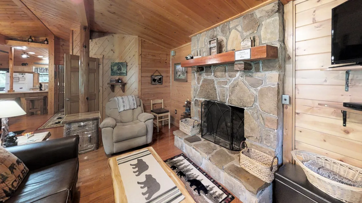 A cozy nook with a stone fireplace, a comfortable armchair, wood accents, and a decorative textile rug. This corner is designed for relaxation, reading, or socializing in a secure and peaceful setting.