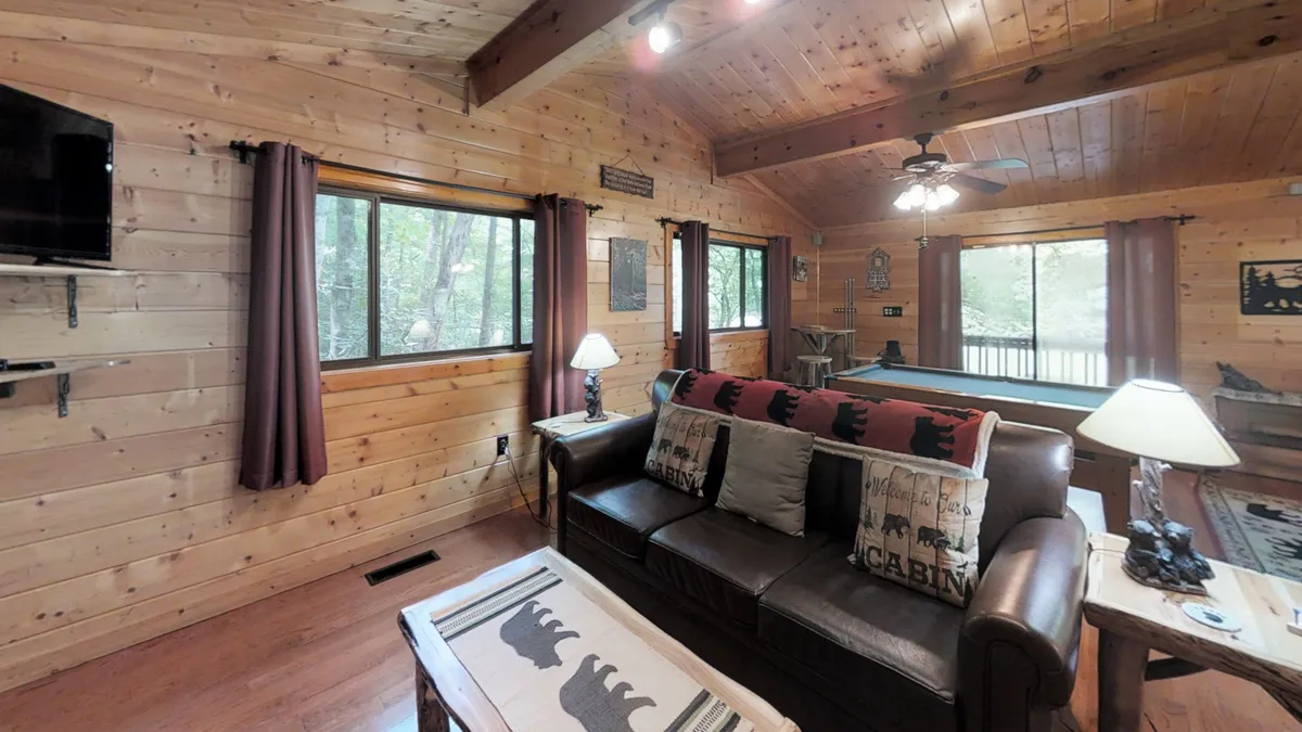 A warmly lit living area featuring a leather sofa, a wooden coffee table, and large windows that fill the space with natural light. Decorative pillows and rustic finishes contribute to a cozy, inviting atmosphere that feels both private and comfortable.