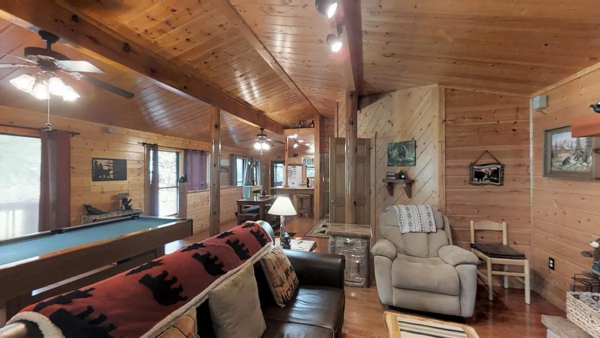 Inside the cabin, a stylish game room invites guests to play pool or relax on a sofa beneath a warm wooden ceiling and modern light fixtures. The room exudes both comfort and entertainment—ideal for evening leisure after a day out.