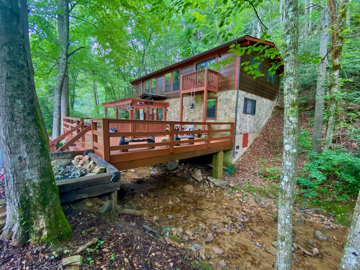 A spacious wooden deck with scenic stone exterior, set amidst tall trees and with a stream flowing nearby. The deck is perfect for relaxing, enjoying nature walks, and gathering as a family after a day at local attractions.