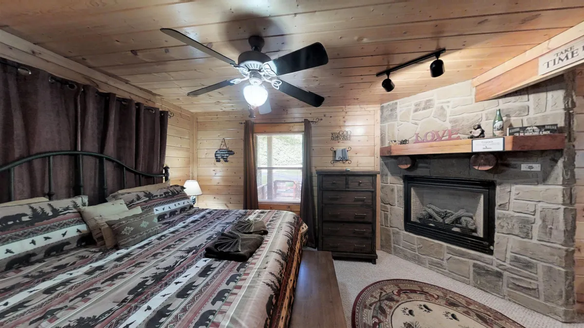 A warmly decorated bedroom featuring a bed with patterned bedding, a stone fireplace, and rustic wooden furniture. Soft lighting and natural materials create a cozy and restful ambiance.