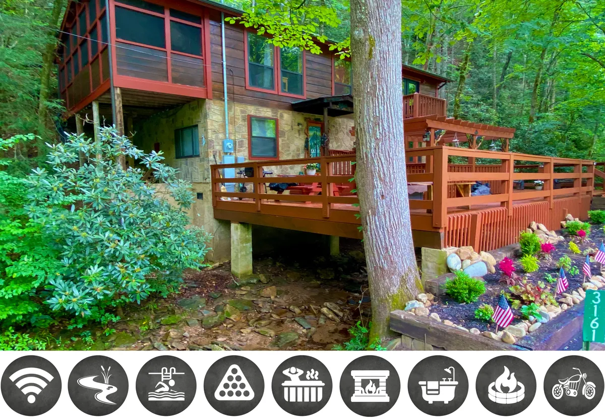 The image showcases the cabin’s inviting wooden deck set against a stone exterior, framed by large windows that reflect the lush greenery all around. The deck offers sunset views and ample space for relaxing, outdoor dining, or family gatherings while surrounded by the peaceful sounds of nature.