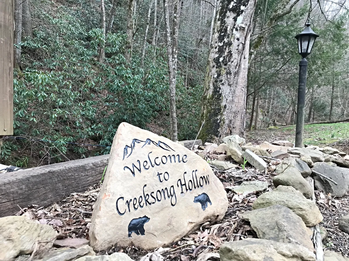 A welcoming sign set on a rock greets visitors upon arrival, surrounded by natural landscape and a lamp post. The scene feels inviting and hints at the start of an adventure in the Smoky Mountains.