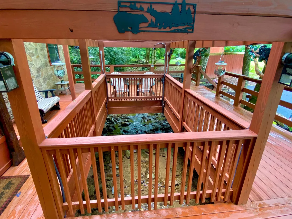 A spacious wooden deck overlooks serene greenery, with decorative lanterns and a unique sculpture accentuating the peaceful vibe. The scene suggests opportunities for enjoying the water, reading, or hosting outdoor events in a beautiful natural setting.