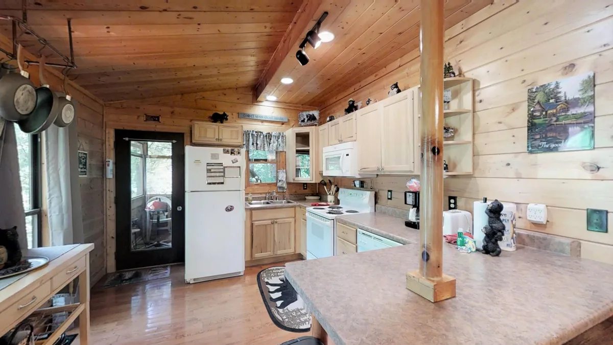 A well-equipped, modern kitchen with wooden cabinetry, a central island, stainless appliances, decorative elements, and windows letting in natural light. The space is open and conducive to group meal preparation and casual conversation.