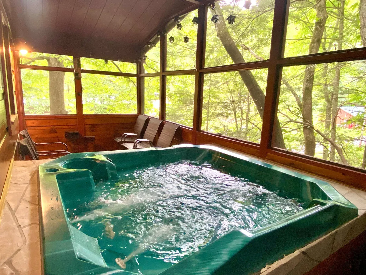 This interior image features a spacious room with a large, inviting hot tub positioned near broad windows. The room is adorned with warm wooden paneling and offers a tranquil seating area, allowing guests to relax while gazing out at the surrounding nature.